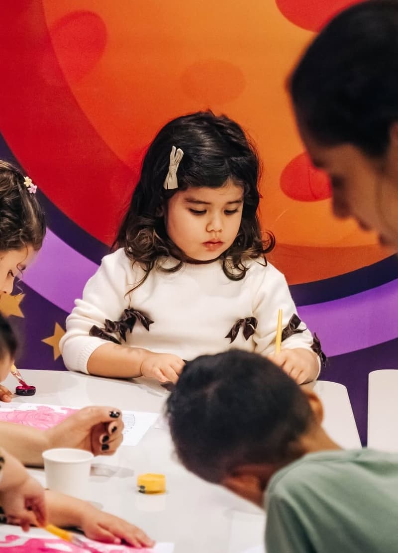Crianças pintando na mesa com as voluntárias da Estação Rocket